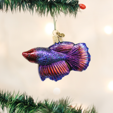 Glittery purple and red glass Betta Fish ornament hanging from a green Christmas tree branch.