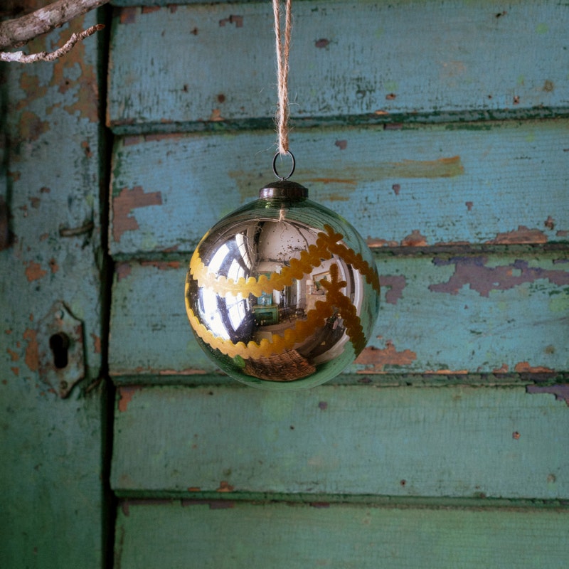 Venetian Glass 5-inch silver ball ornament with yellow scalloped patterns on a rustic blue door.