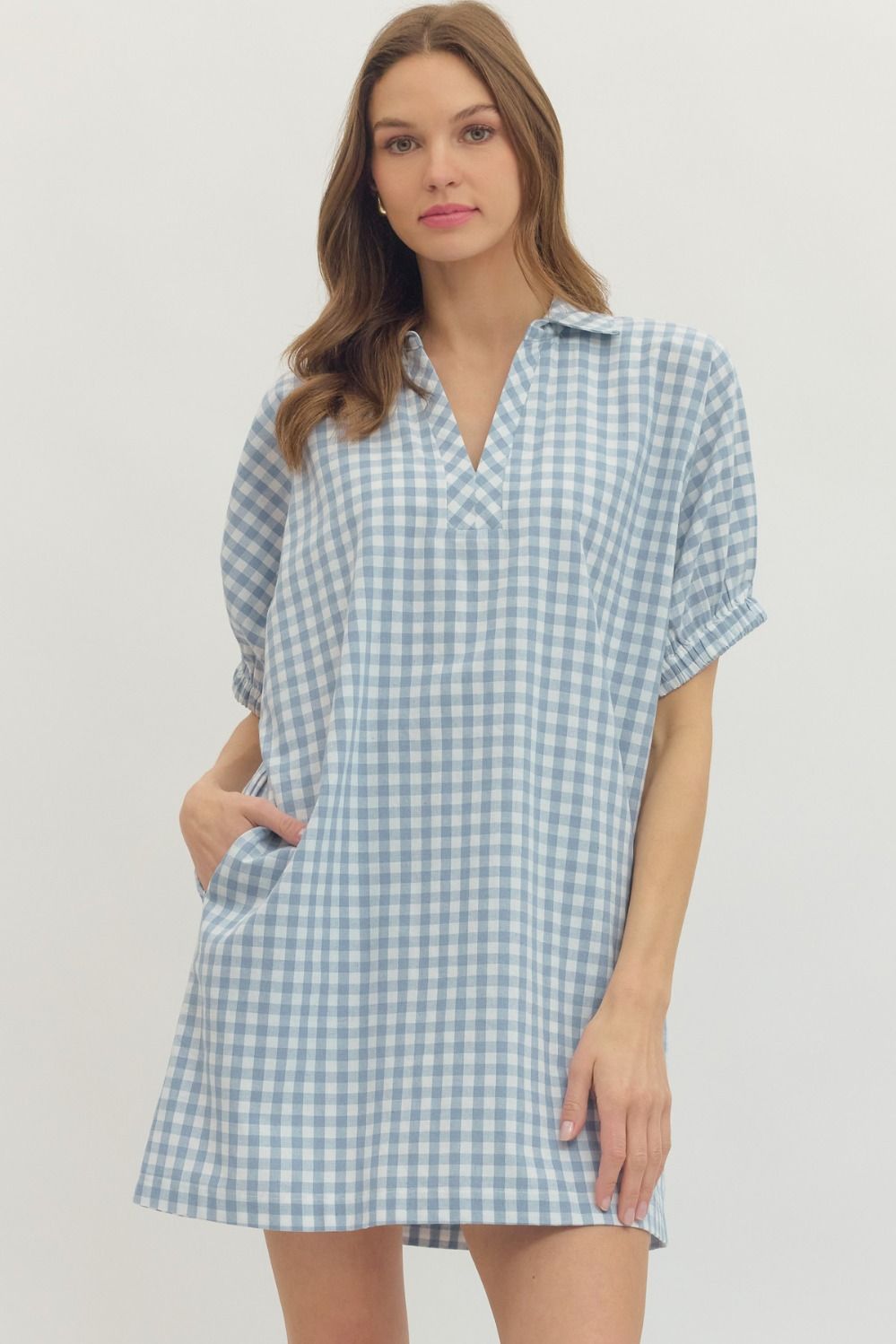 Woman wearing the Naomi Gingham Short Sleeve Mini Dress in light blue and white with side pockets.