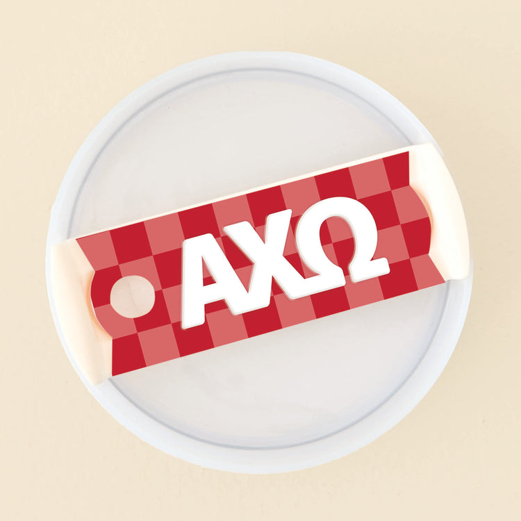 Red and white checkered acrylic tumbler lid tag featuring white Greek letters AXΩ.