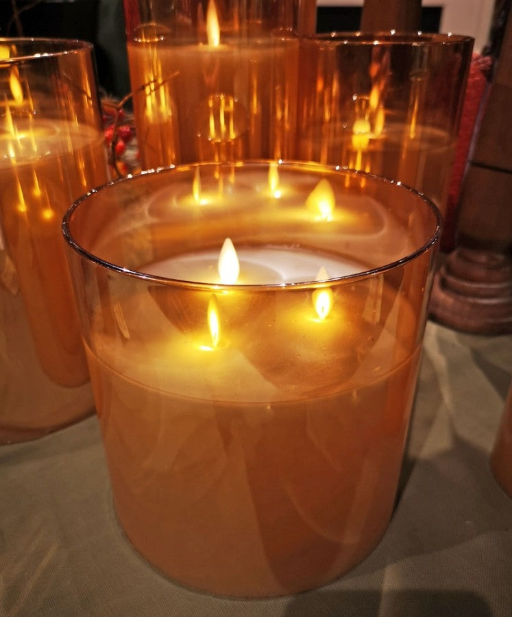 Amber glass 3-wick candle glowing with warm light on a table.