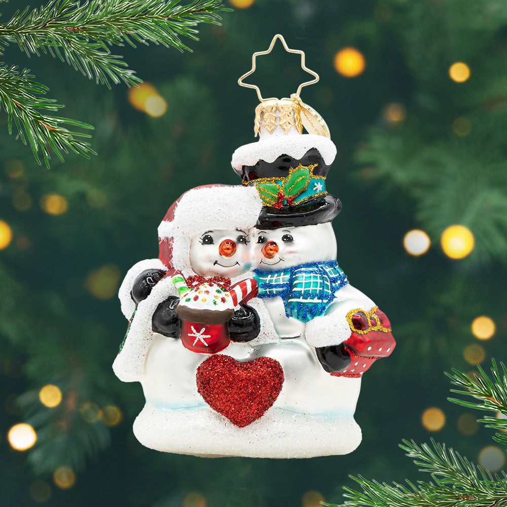 Glass Christmas ornament of two snowmen hugging, holding a red heart and a cup of cocoa.