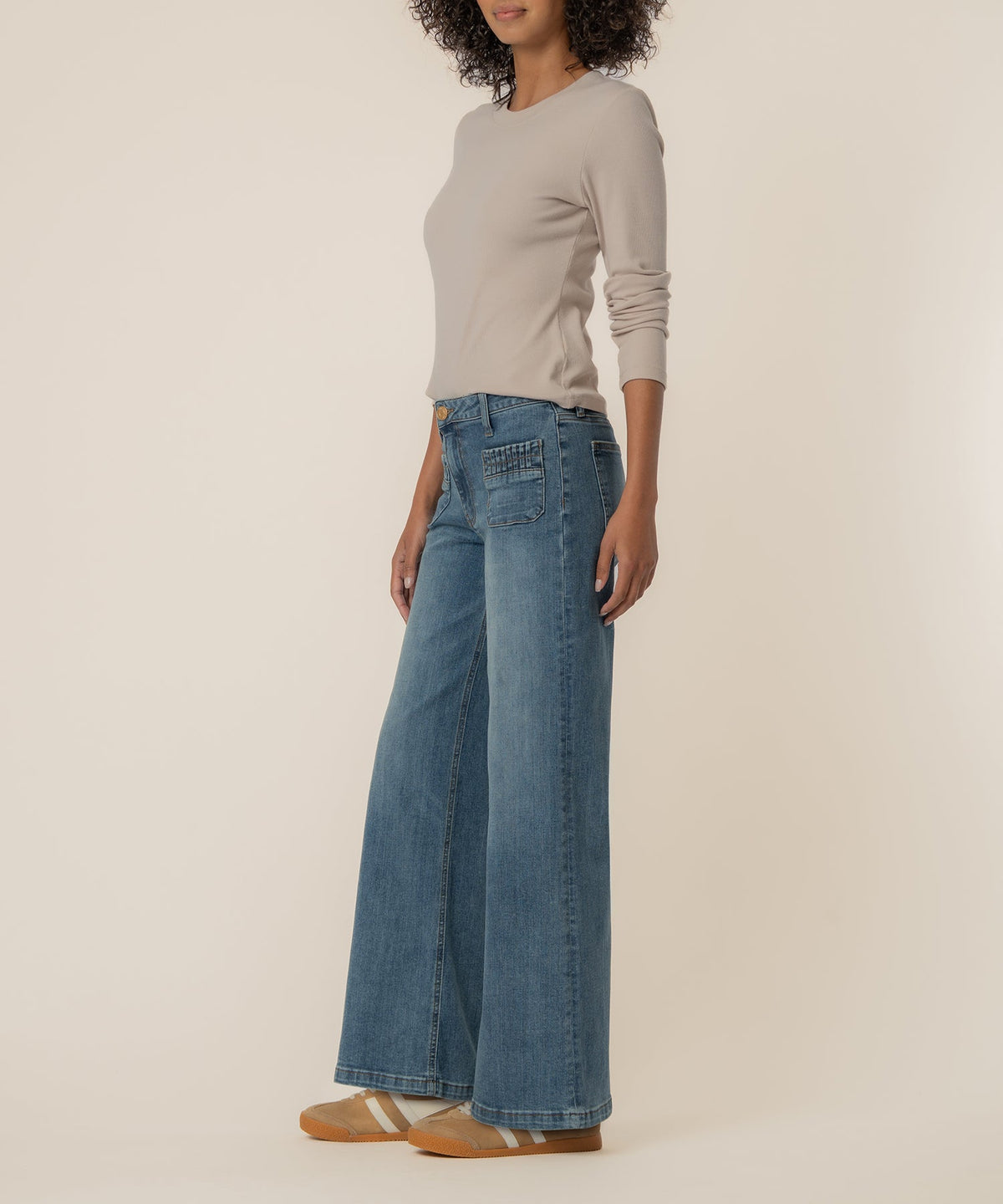 Woman wearing Maya high-rise wide-leg jeans with ruched patch pockets and a beige long-sleeve top.