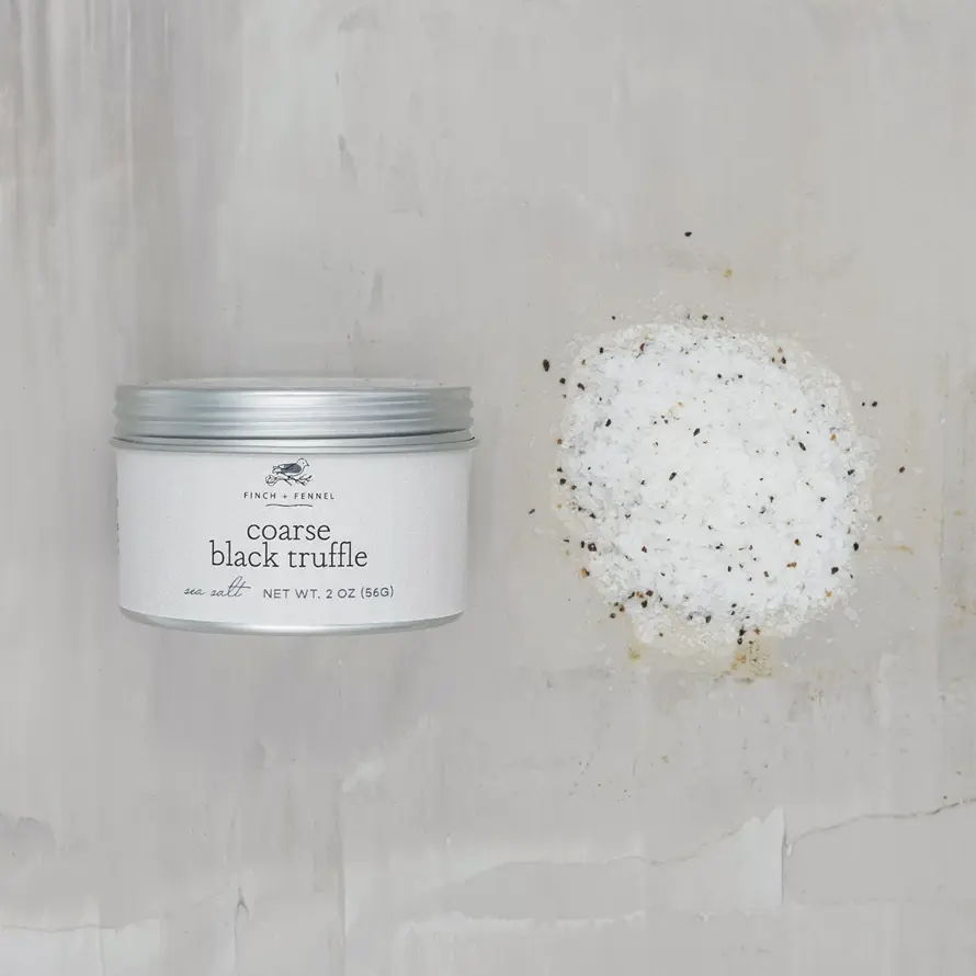 Coarse black truffle sea salt in a cylindrical glass jar with a metal lid.