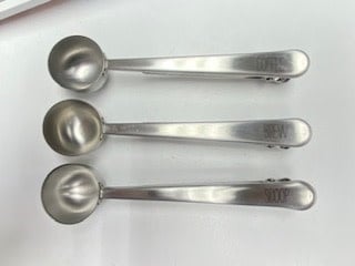 Stainless steel coffee scoop with printed sentiment text on a bag clip handle.