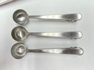 Stainless steel coffee scoop with printed sentiment text on a bag clip handle.