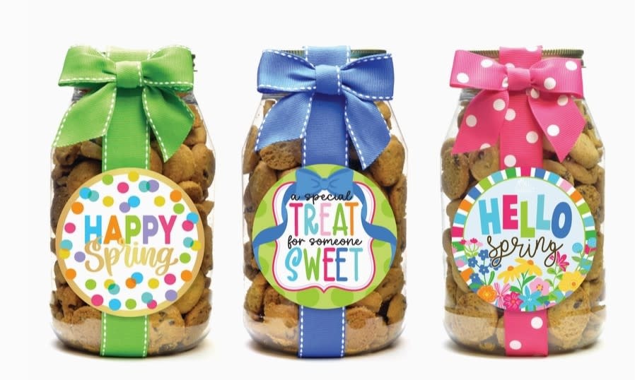 Three glass jars filled with cookies, each featuring a unique spring-themed label and ribbon bow.