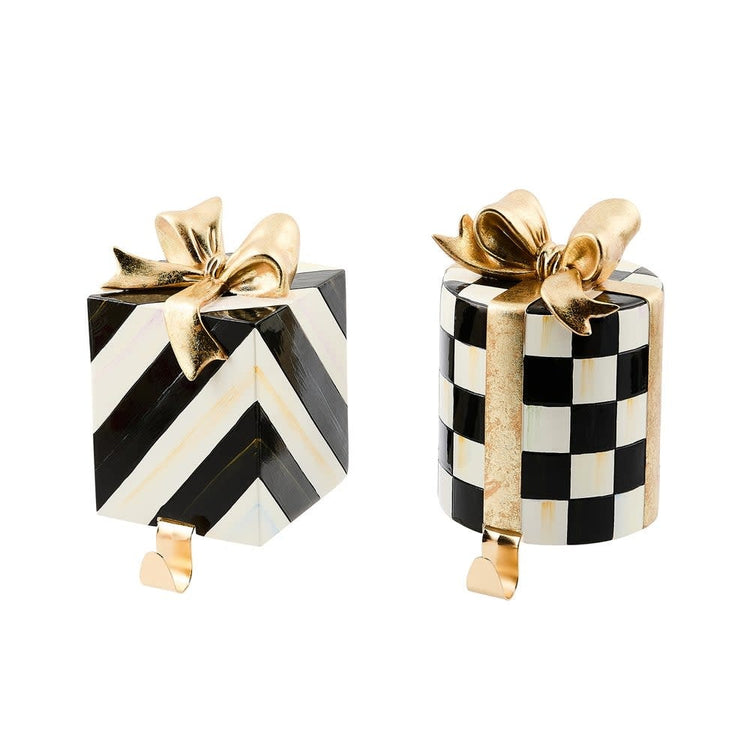 Resin stocking holder shaped like a gift box with gold ribbon detail in classic Christmas colors.