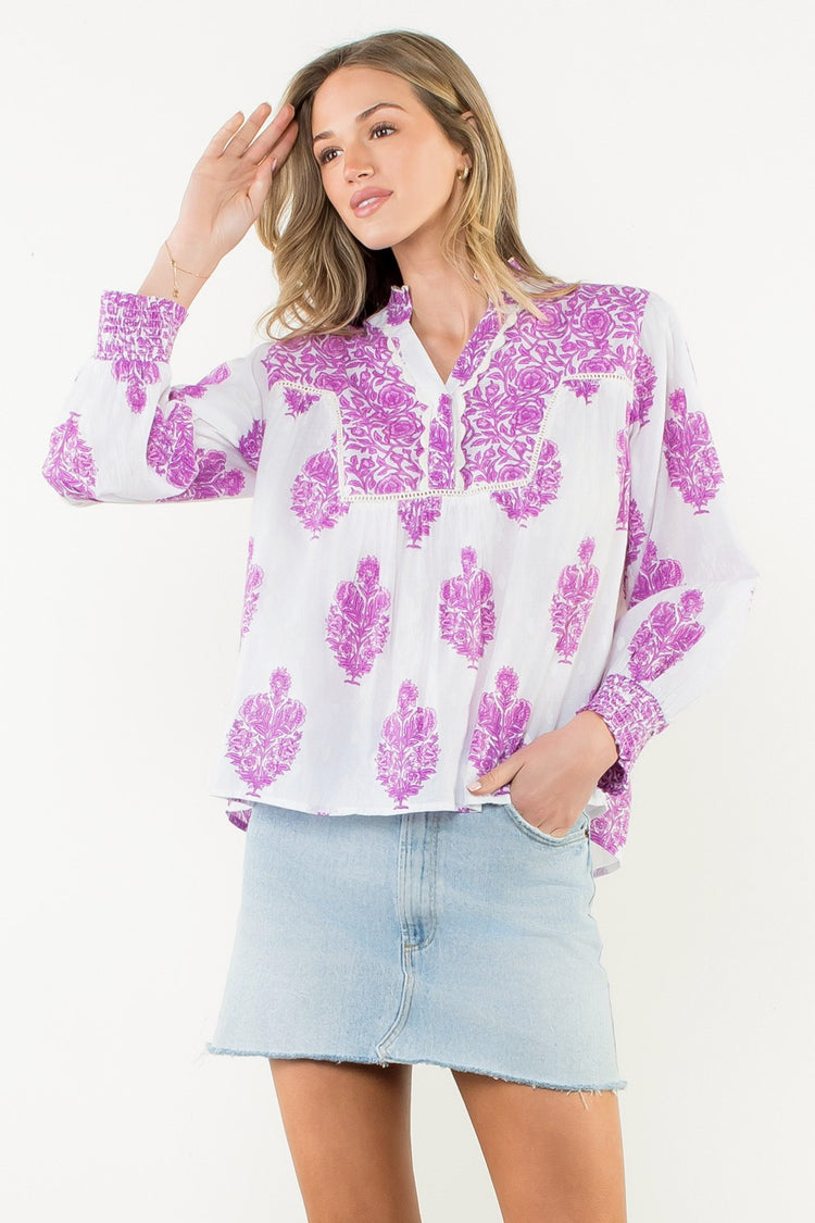 Woman wearing the Amy Long Sleeve Flower Print Top in white with purple floral patterns.