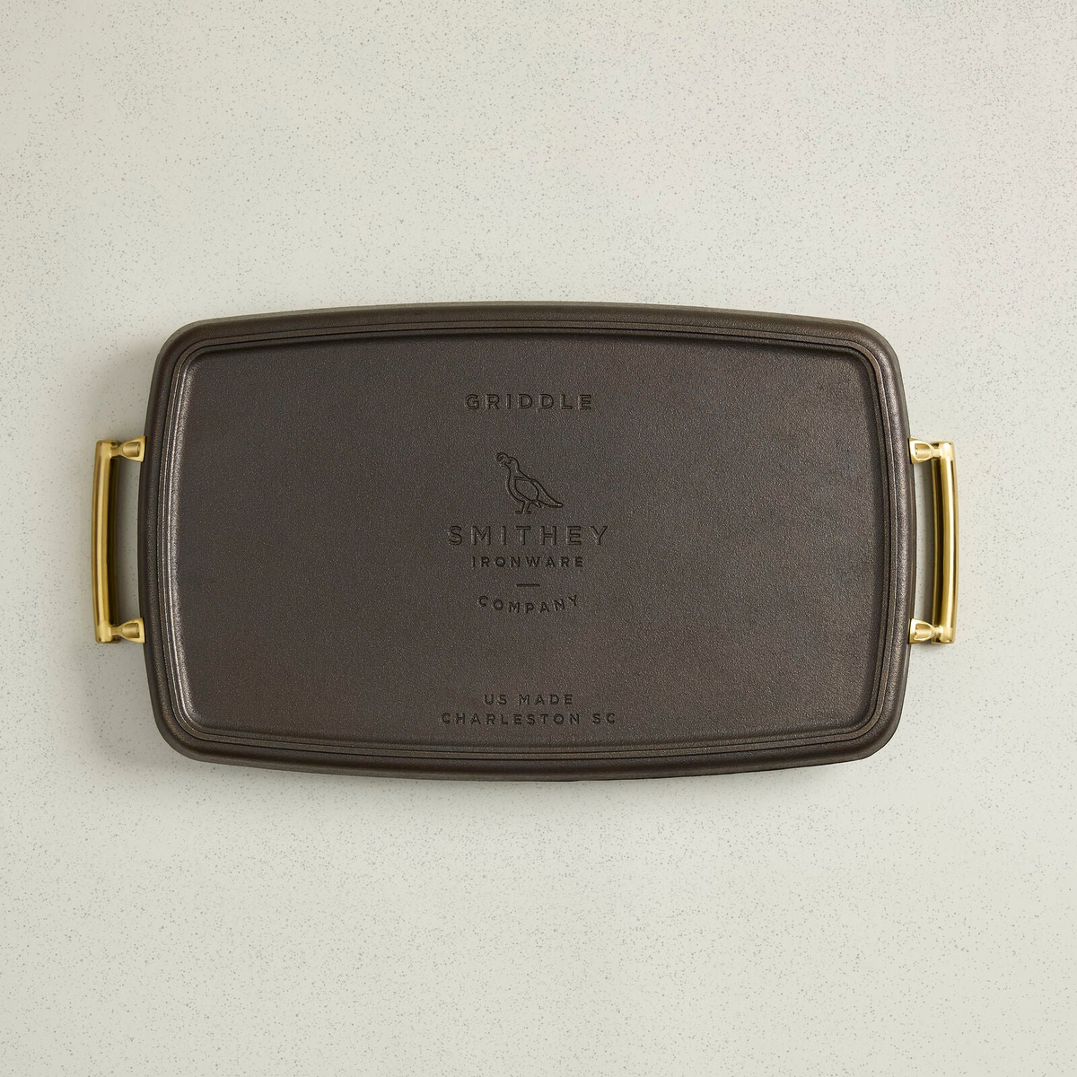Top view of a rectangular cast iron double burner griddle with gold-toned side handles.