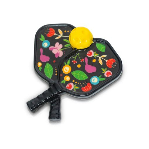 Black pickleball paddles with a colorful floral and bunny pattern, topped with a yellow pickleball.