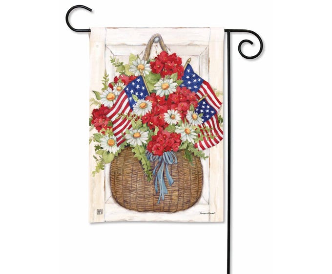 Garden flag with a basket of red flowers, daisies, and American flags against a white wooden background.