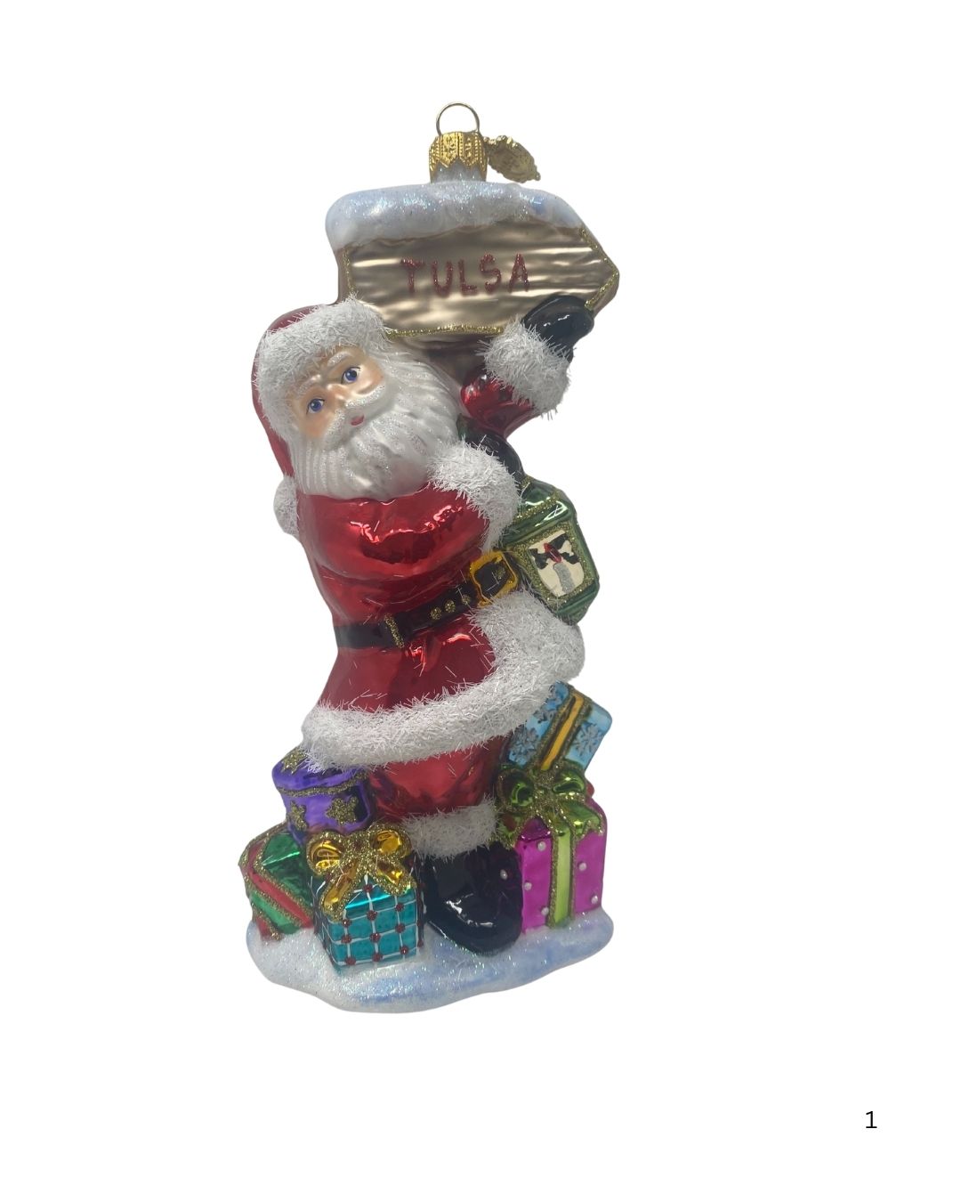 Glass Santa ornament holding a Tulsa sign and lantern, standing over colorful gift boxes.