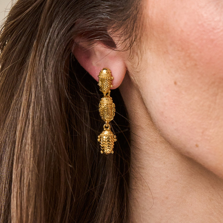 Close-up of a person wearing gold Scarab Petite Linear Earrings with three tiered scarab charms.