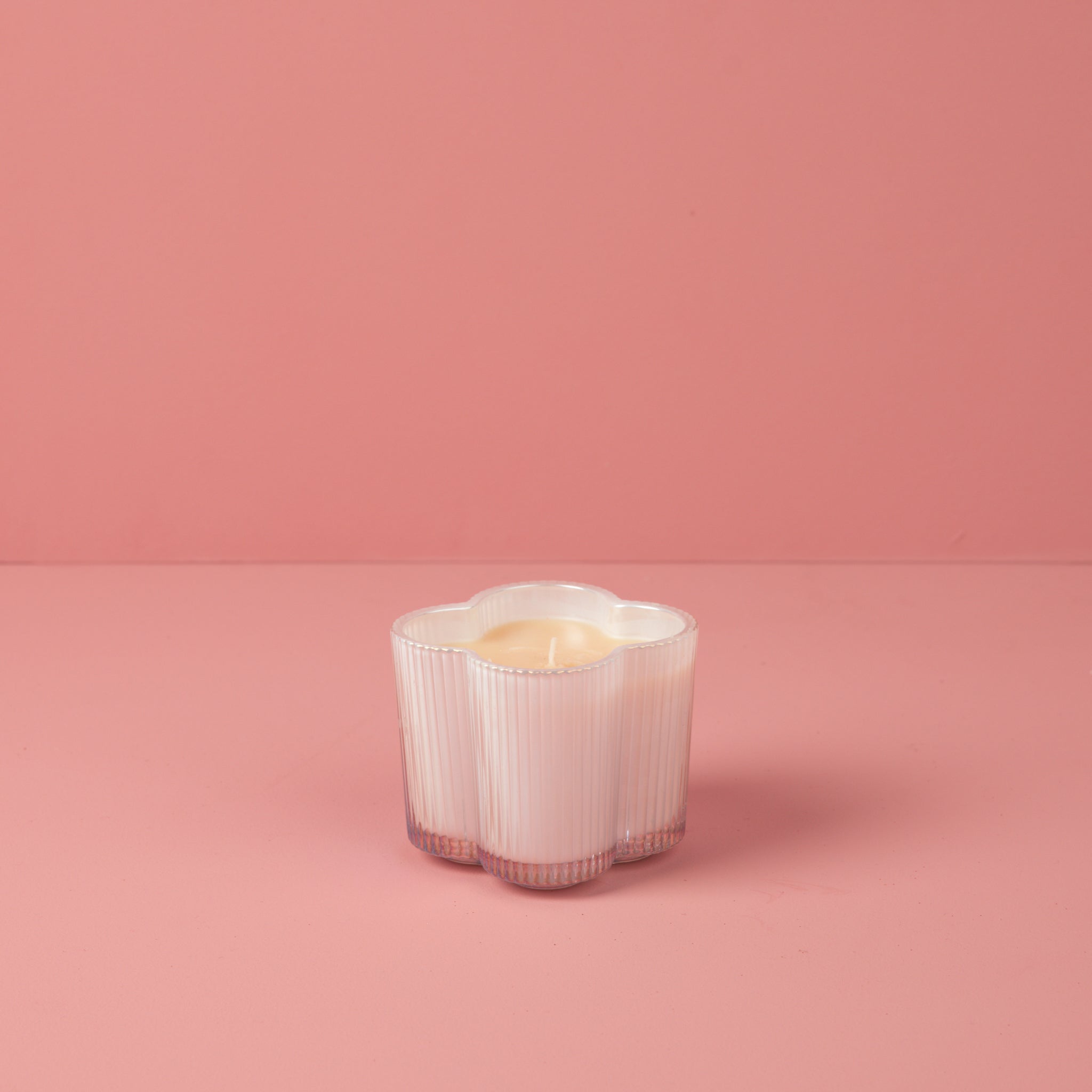 Sweet Grace #076 candle in an iridescent white flower-shaped ribbed glass jar on a pink background.