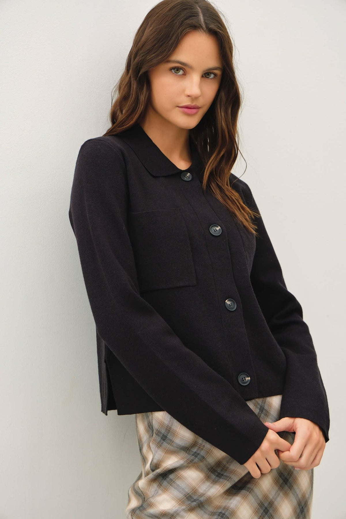 Black cropped knit jacket with collared neckline, functional buttons, large chest patch pockets, and tailored silhouette.