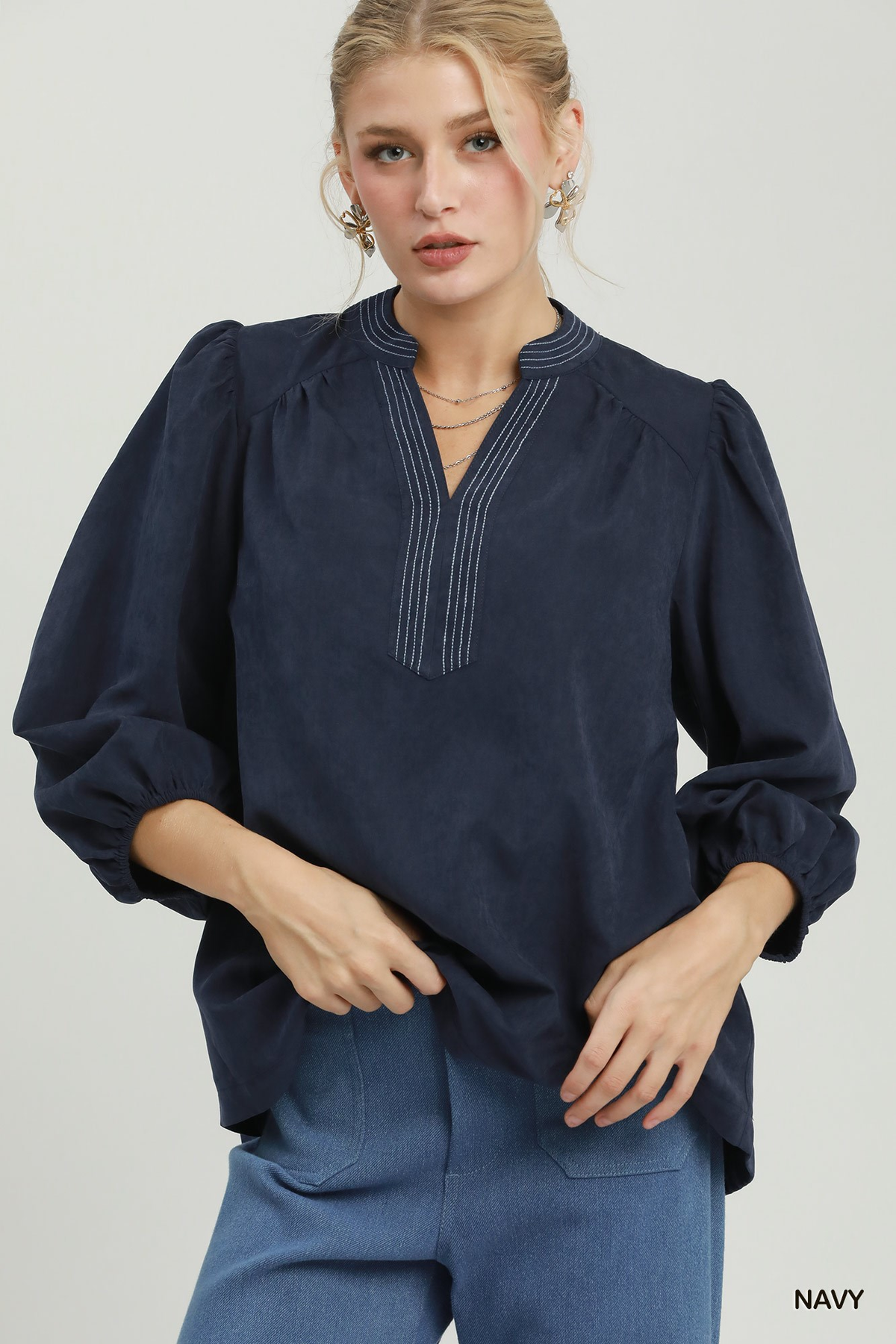 Woman wearing a navy Clara Sueded Split Neck Blouse with contrast stitching and puff sleeves.