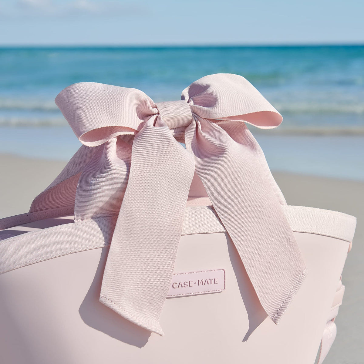 Ballet pink insulated cooler tote with a large decorative bow on the handle at the beach.