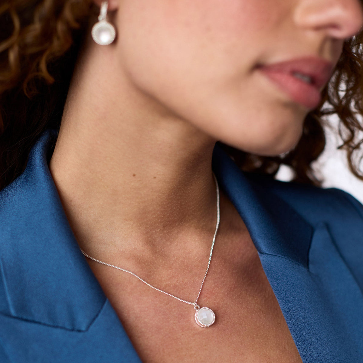 A woman wearing the Fleur-de-Lis Solitaire Silver Necklace with a round white glass pendant.
