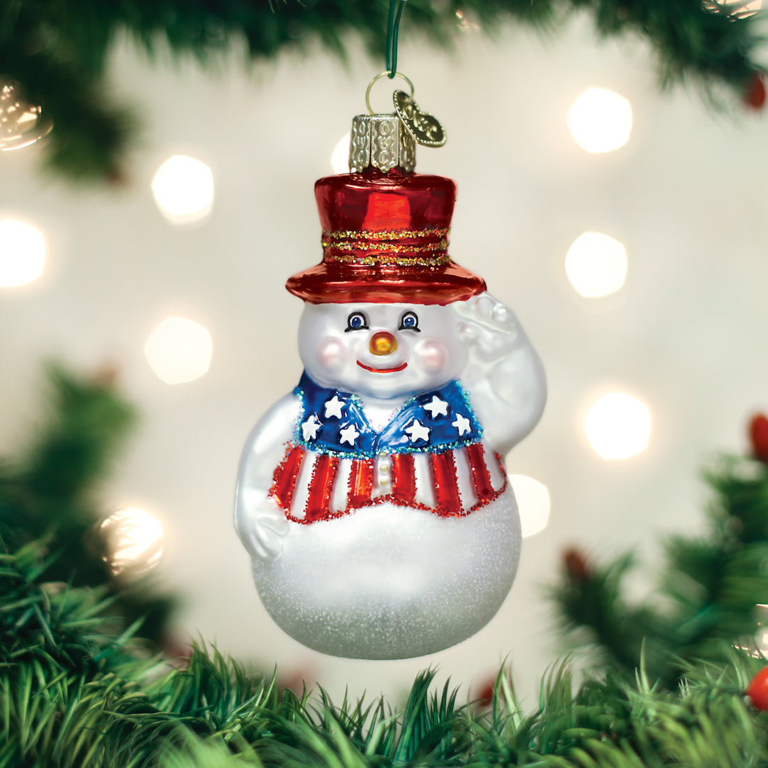 Patriotic snowman glass ornament with a red top hat and American flag vest on a Christmas tree.