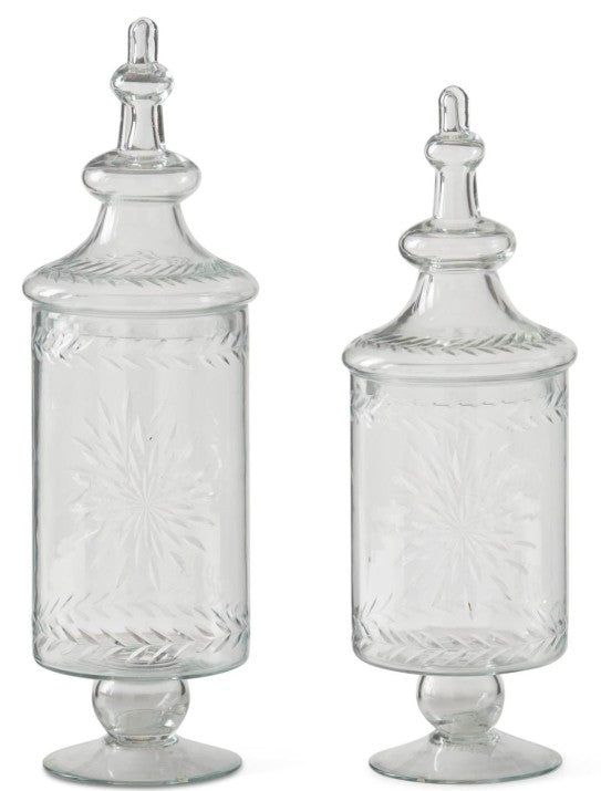 Two clear glass apothecary jars with etched starburst designs and decorative lids on pedestal bases.
