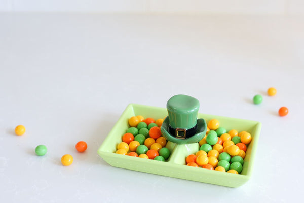 Green ceramic divided dish with a leprechaun hat centerpiece filled with green, orange, and yellow candies.