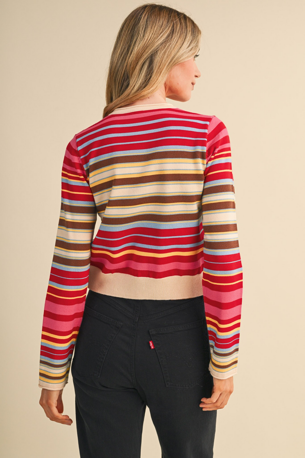 Back view of a woman wearing a multi-color striped sweater cardigan and black jeans.