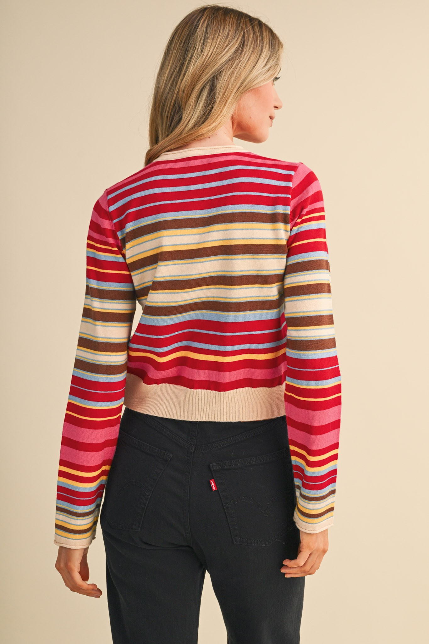 Back view of a woman wearing a multi-color striped sweater cardigan and black jeans.