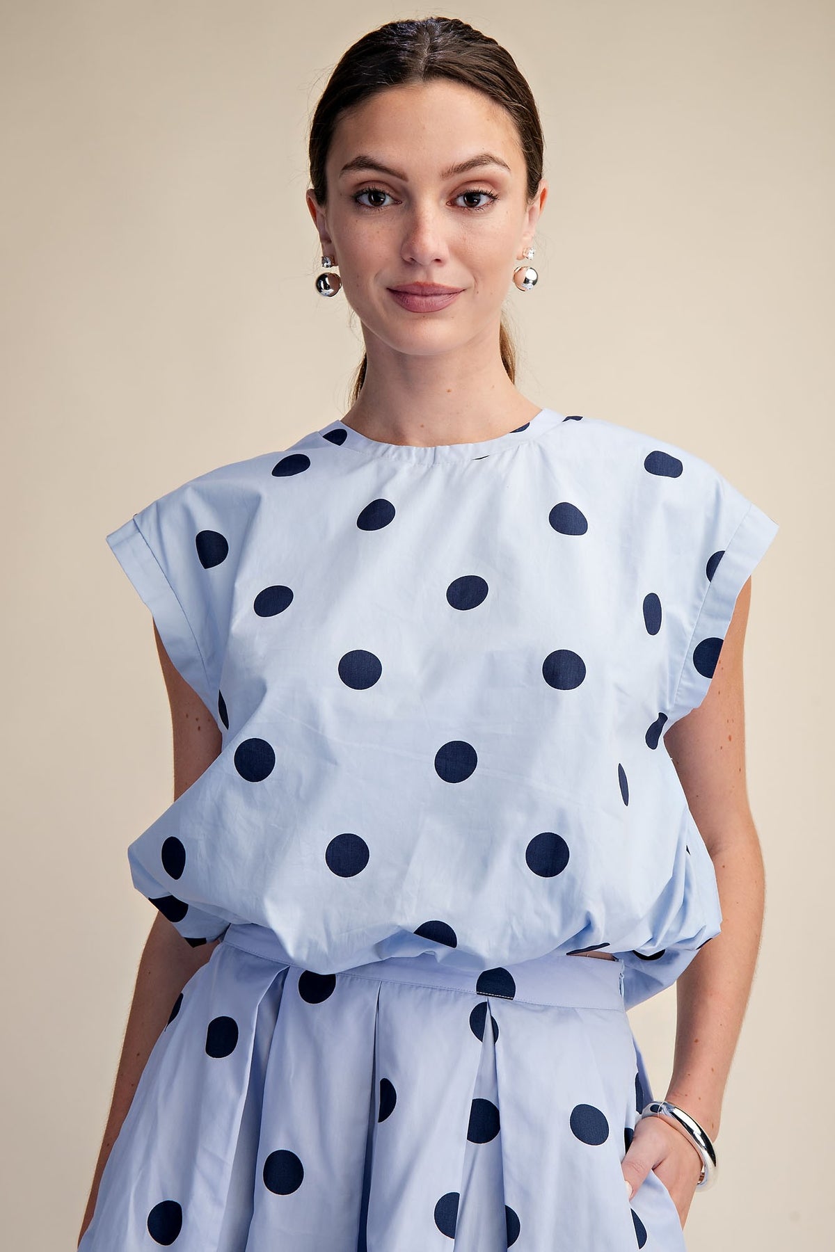 Woman wearing a light blue Cindy round neck bubble crop top with large navy polka dots.