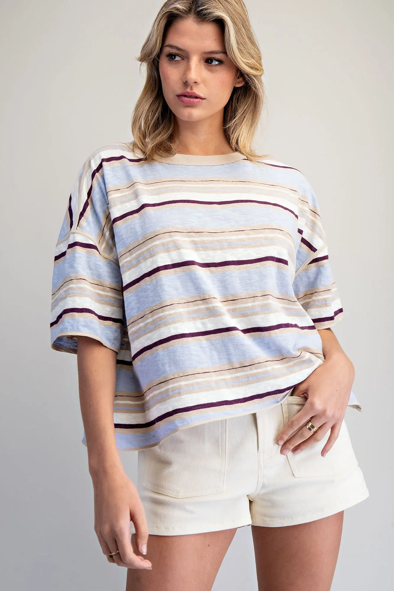 Woman wearing the Elena Striped Boxy T-Shirt in a blue, tan, and purple horizontal stripe pattern.