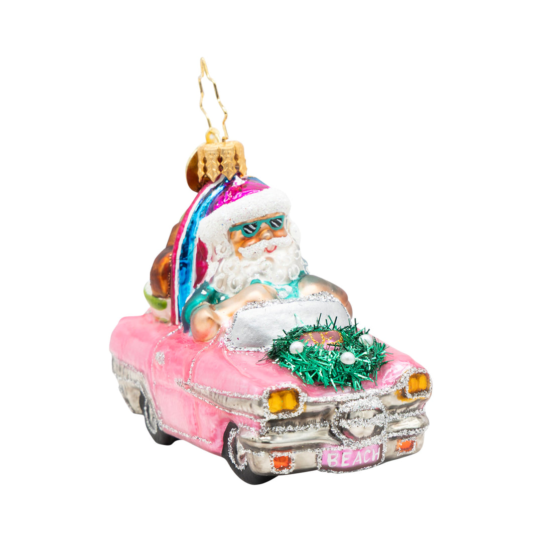 Santa in sunglasses driving a pink convertible with a surfboard and beach gear ornament.