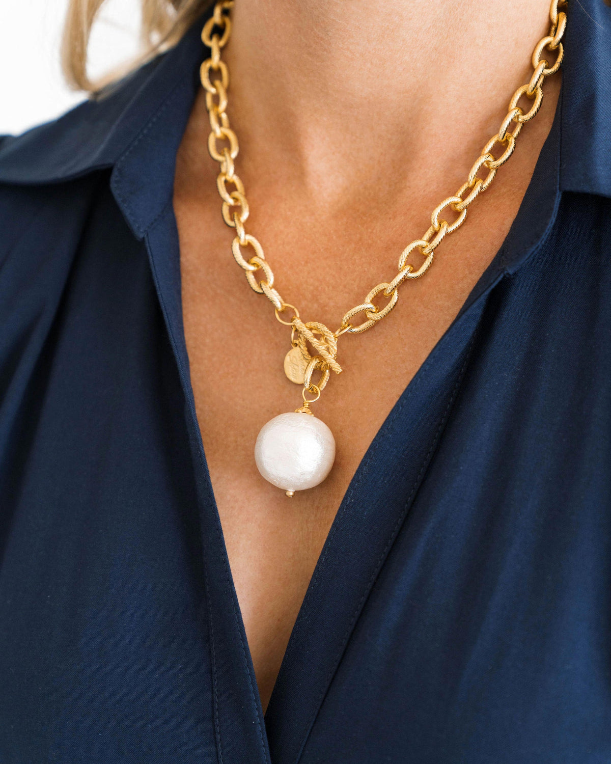 A person wearing a gold cotton pearl toggle necklace with a chunky chain and large white pearl.