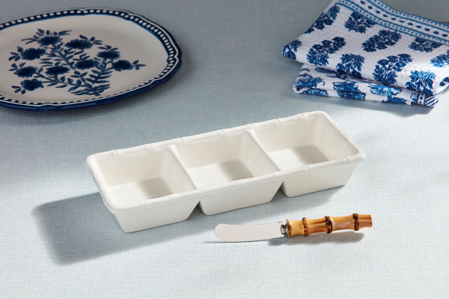 White ceramic triple tidbit dish with bamboo-style trim and a matching bamboo-handled spreader.