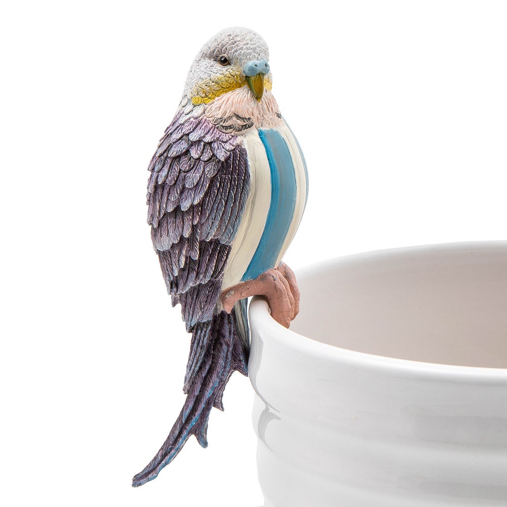 Blue and purple resin parakeet pot climber figurine perched on the edge of a white ceramic pot.
