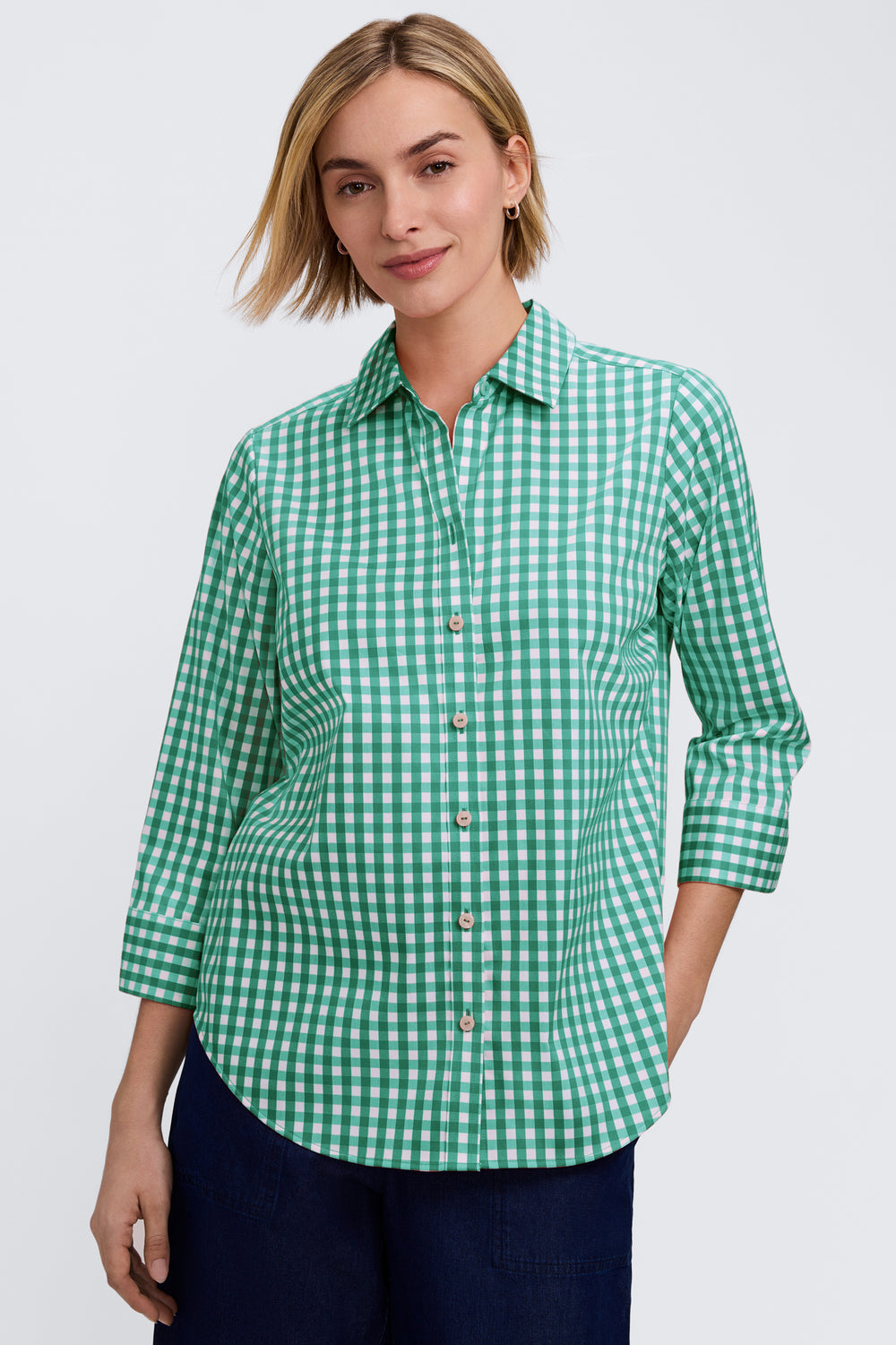 Woman wearing a green and white gingham 3/4 sleeve button-front shirt with a rounded hem.