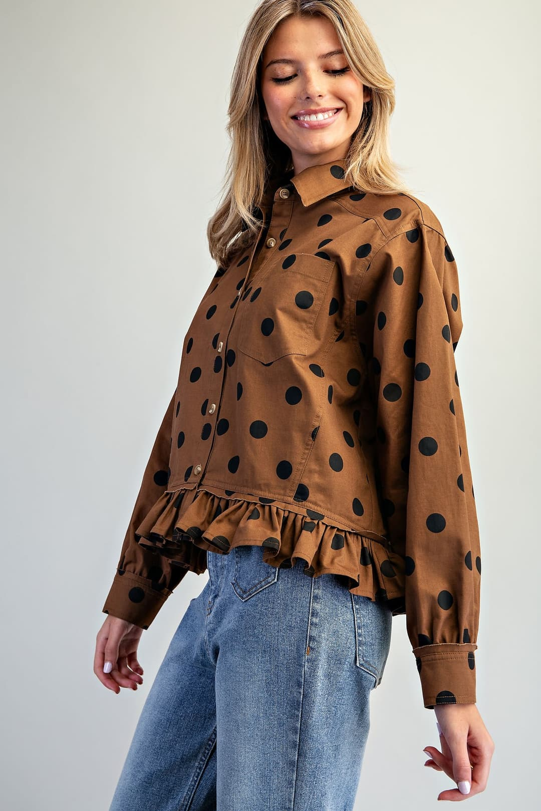 Woman wearing a brown polka dot button-down blouse with a ruffled hem and blue jeans.