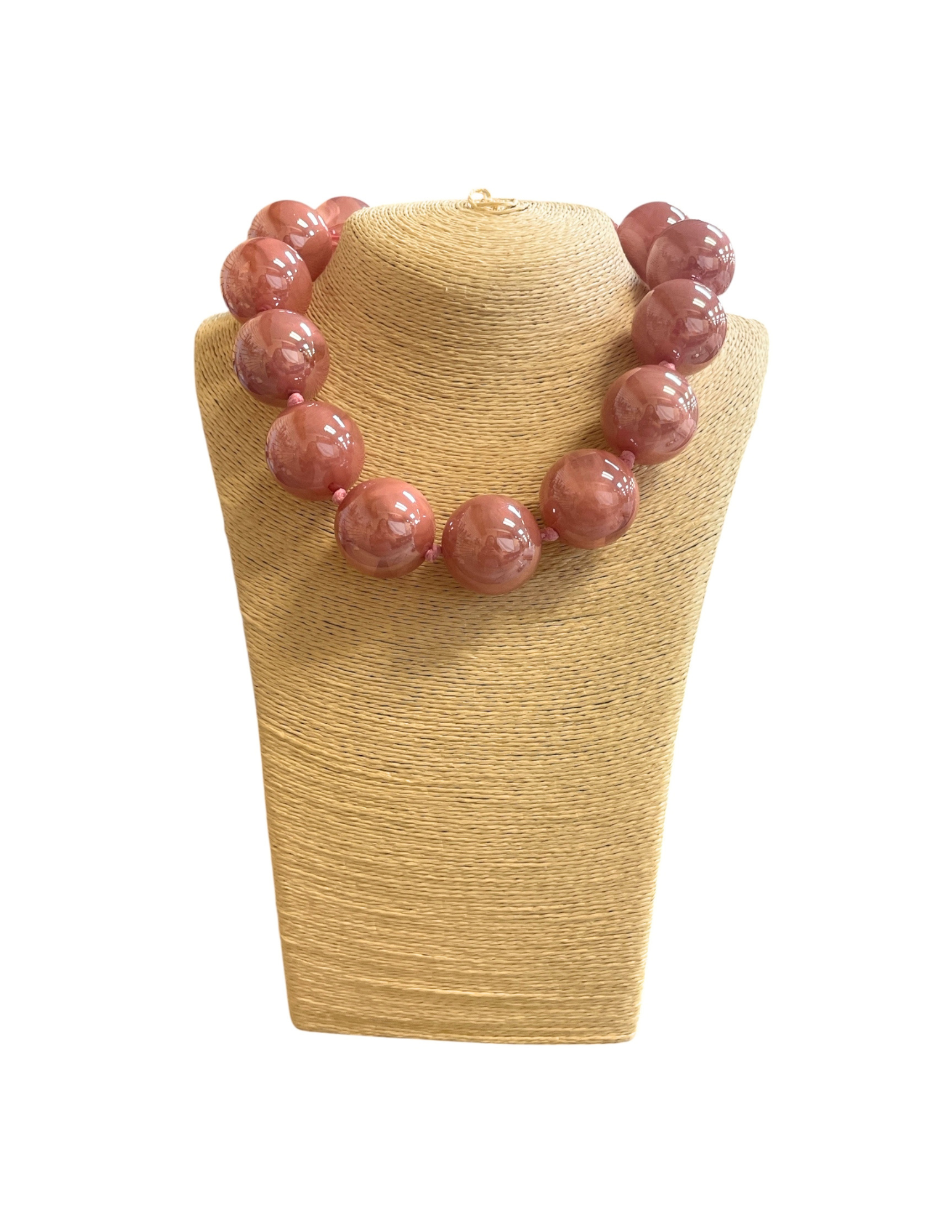 Short necklace with large, glossy pink glass ball beads on a tan woven jewelry display stand.