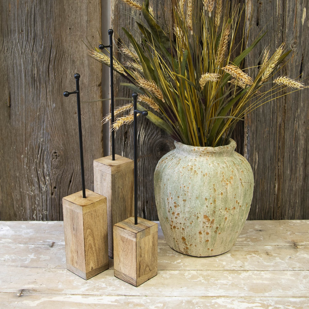 Three black metal mini gallery display stakes in varying heights on wooden blocks next to a vase.