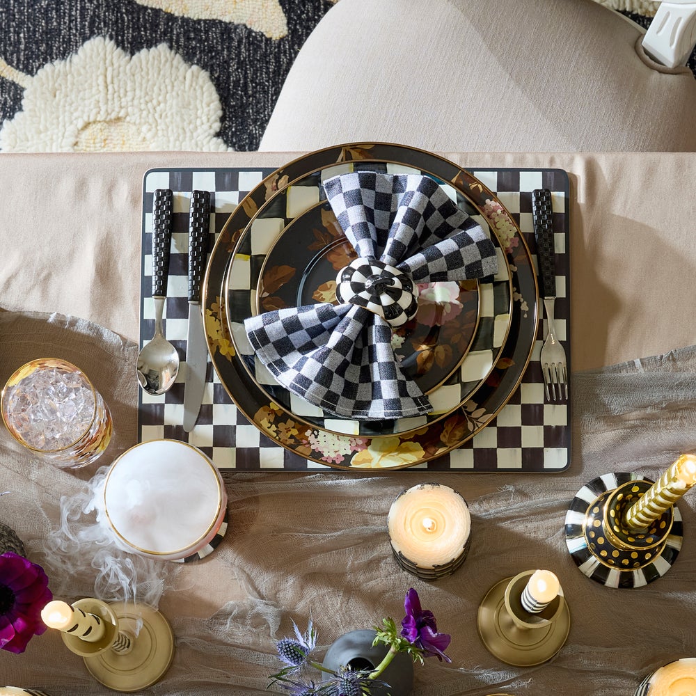 A black and white checkered cork-back placemat set with floral plates and a checkered napkin.