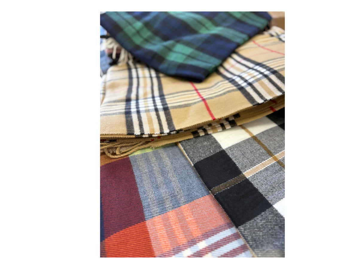 A stack of folded Scottish plaid cashmere scarves in various colors including tan, green, and red.