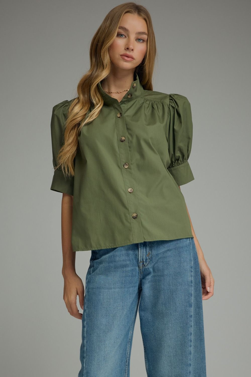 Woman wearing the Delia olive green short puff sleeve button-down top with blue jeans.