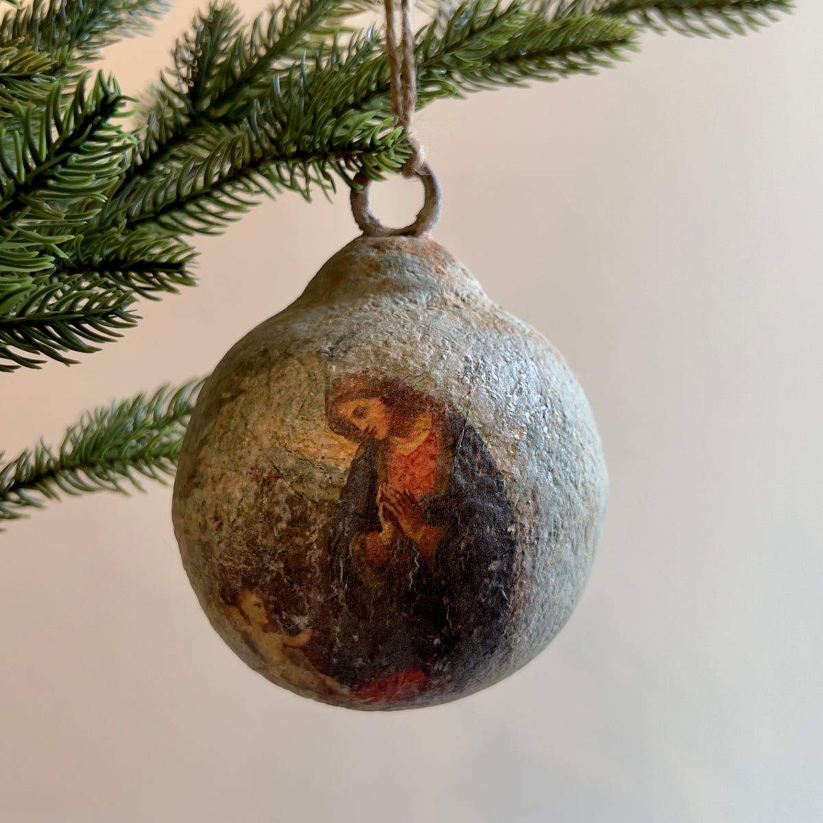 Aged metal ball ornament with a vintage Madonna and Child image hanging from a pine branch.