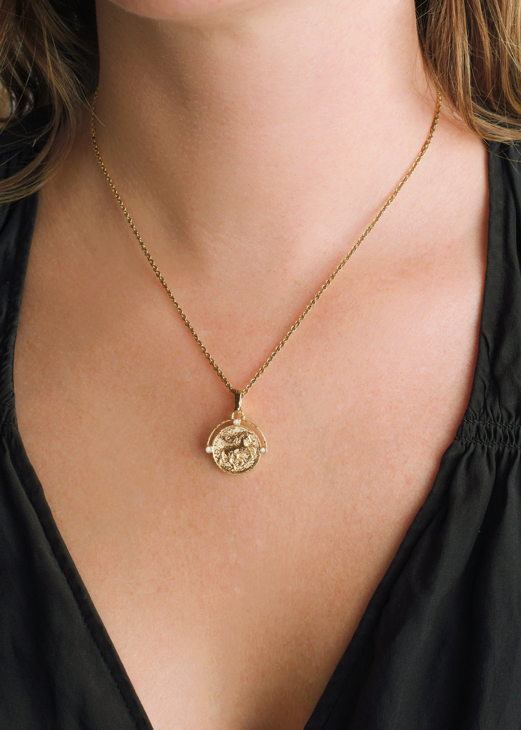 A person wearing the Pegasus Gold Coin Pendant Necklace on an 18K gold plated adjustable chain.