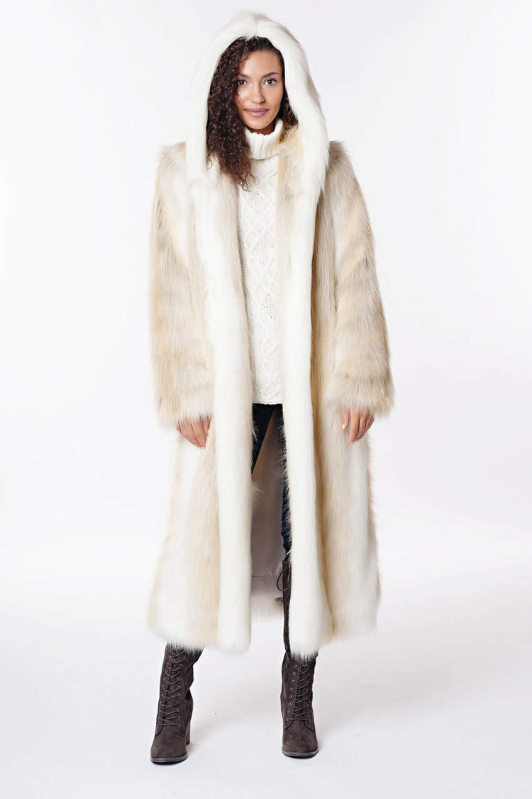 Woman wearing a long, hooded white and cream faux fur coat with a cable knit sweater and boots.