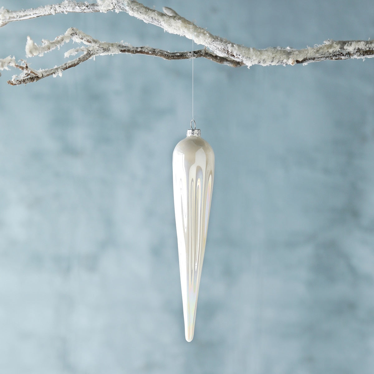 Frosty pearl white glass icicle ornament hanging from a snow-covered branch.
