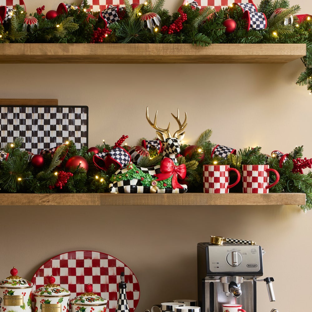 Holly Check Resting Deer figurine with gold antlers and a red bow on a decorated Christmas shelf.