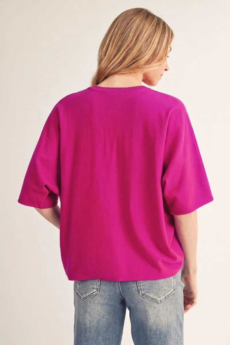 Back view of a woman wearing a bright pink drop shoulder lightweight sweater with blue jeans.