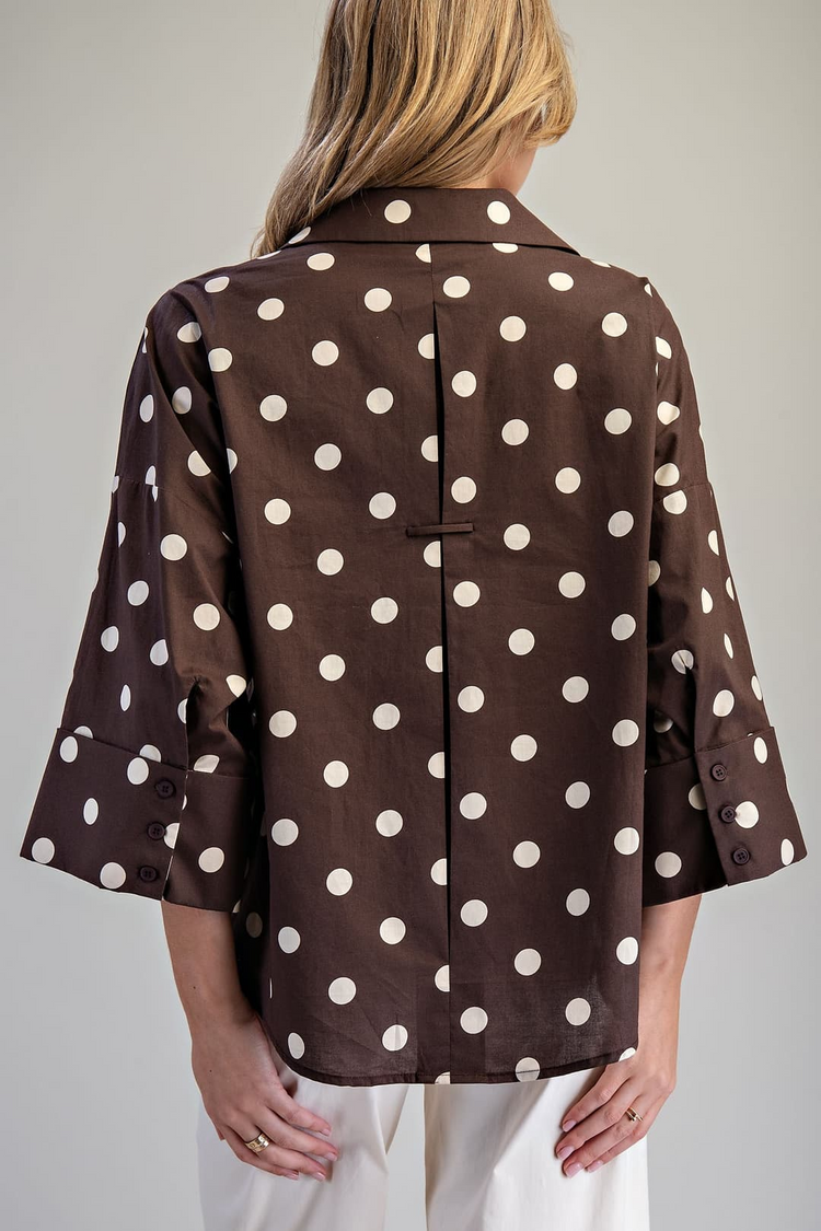 Back view of a brown oversized polka dot blouse with wide dolman sleeves and a pleated back detail.