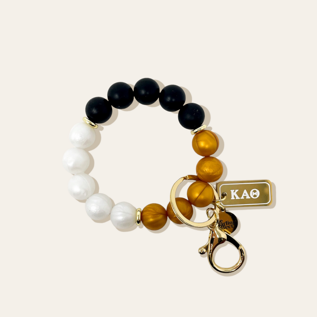 Black, white, and gold beaded keychain wristlet with a gold tag that says KAO.