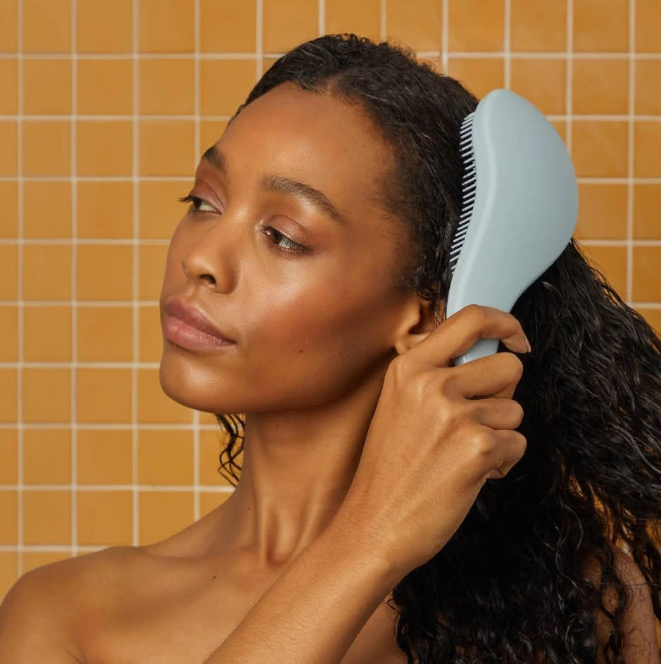 Black detangling brush with flexible bristles designed to smooth tangles.